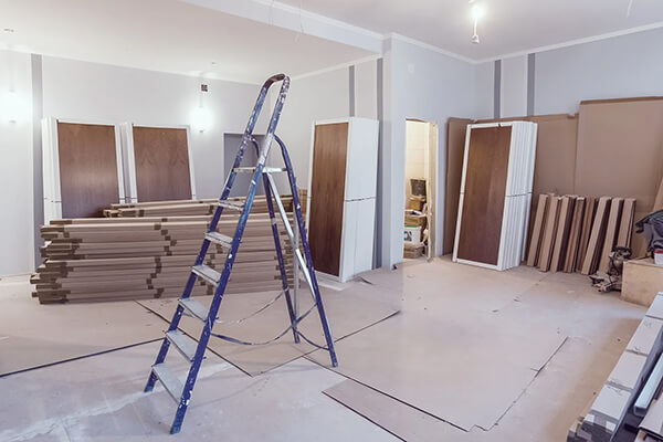 Commercial interior renovation with a ladder, stacked drywall, doors, and construction materials