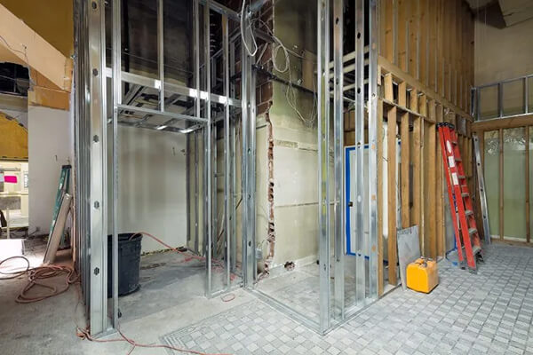 Commercial interior rebuild with exposed metal framing, wall studs, wiring, and construction equipment