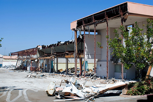 Severely damaged commercial building with exposed framing and debris after a storm