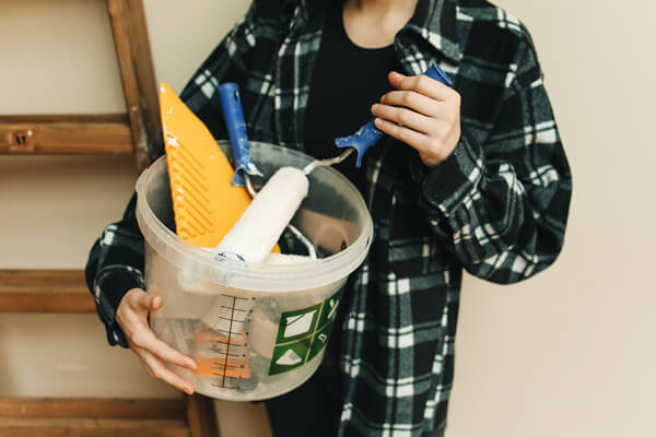 These essential pre-sale renovations can make a big difference. A person holding a bucket with various tools and renovation equipment.
